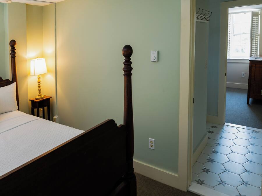 A bedroom with a bed, bedside lamp, and a door leading to another room.