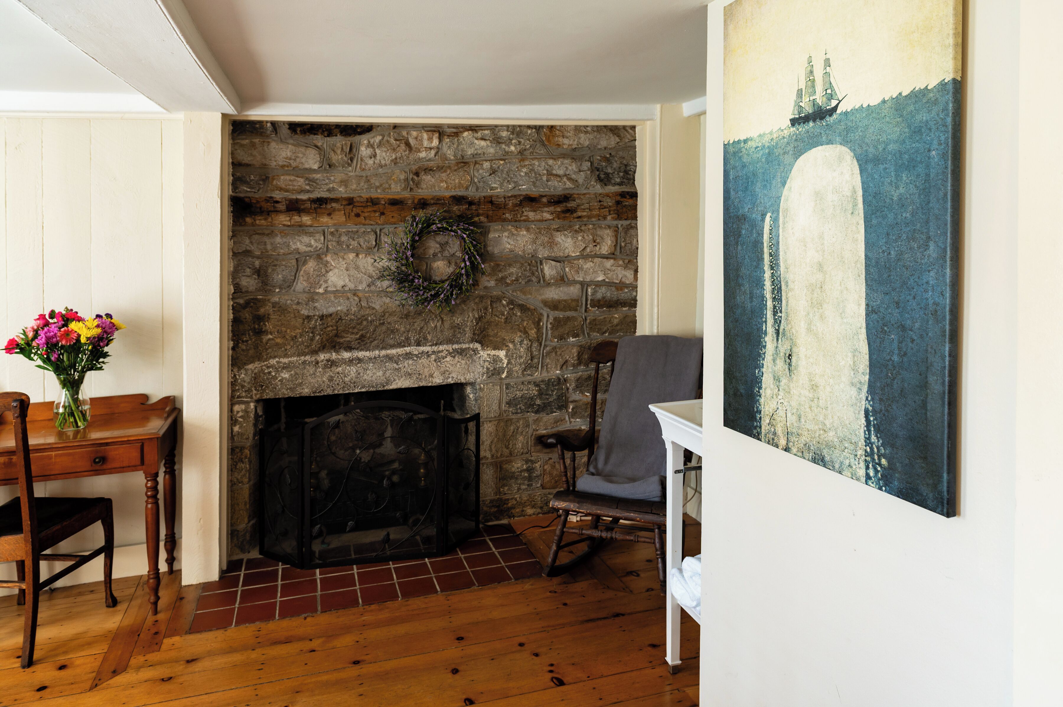 Una habitación con chimenea de piedra, una mesa de comedor de madera con sillas y un cuadro en la pared.