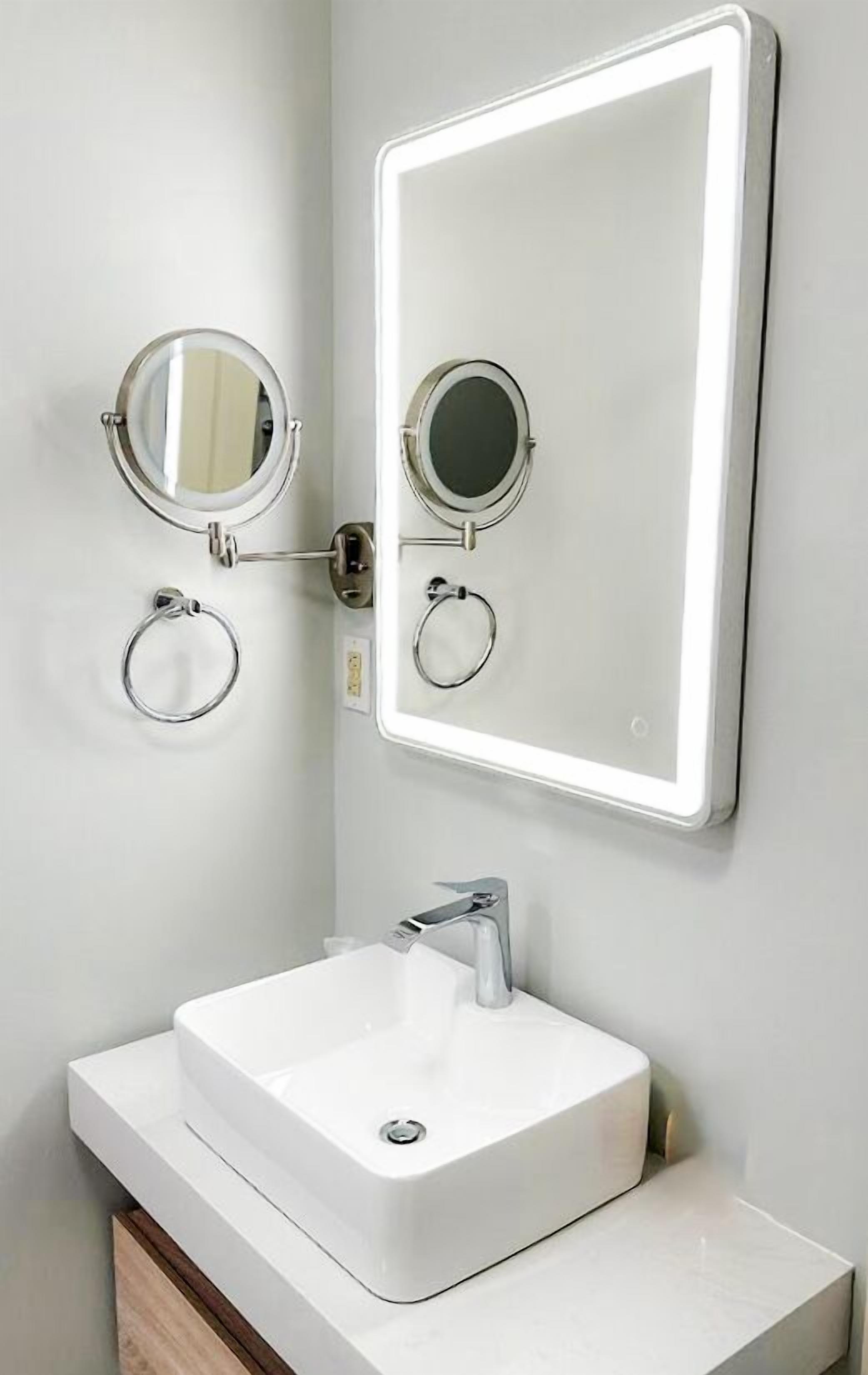 Un baño con un lavamanos blanco, un espejo con luz y dos espejos redondos.