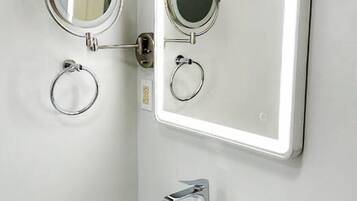 Un baño con un lavamanos blanco, un espejo con luz y dos espejos redondos.