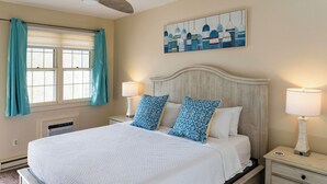 A bedroom with a bed, two bedside lamps, a nightstand, a window with curtains, and a wall painting. - The General Stanton Inn (Charlestown)