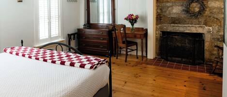 A bedroom with a bed, dresser, chair, desk, and fireplace.