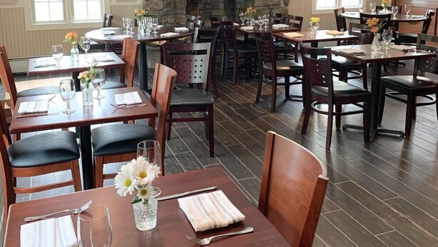 A restaurant with multiple tables and chairs, a stone fireplace, and large windows. - The General Stanton Inn (Charlestown)