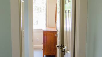 A hallway with a tiled floor leading to a room with a wooden cabinet and a door.