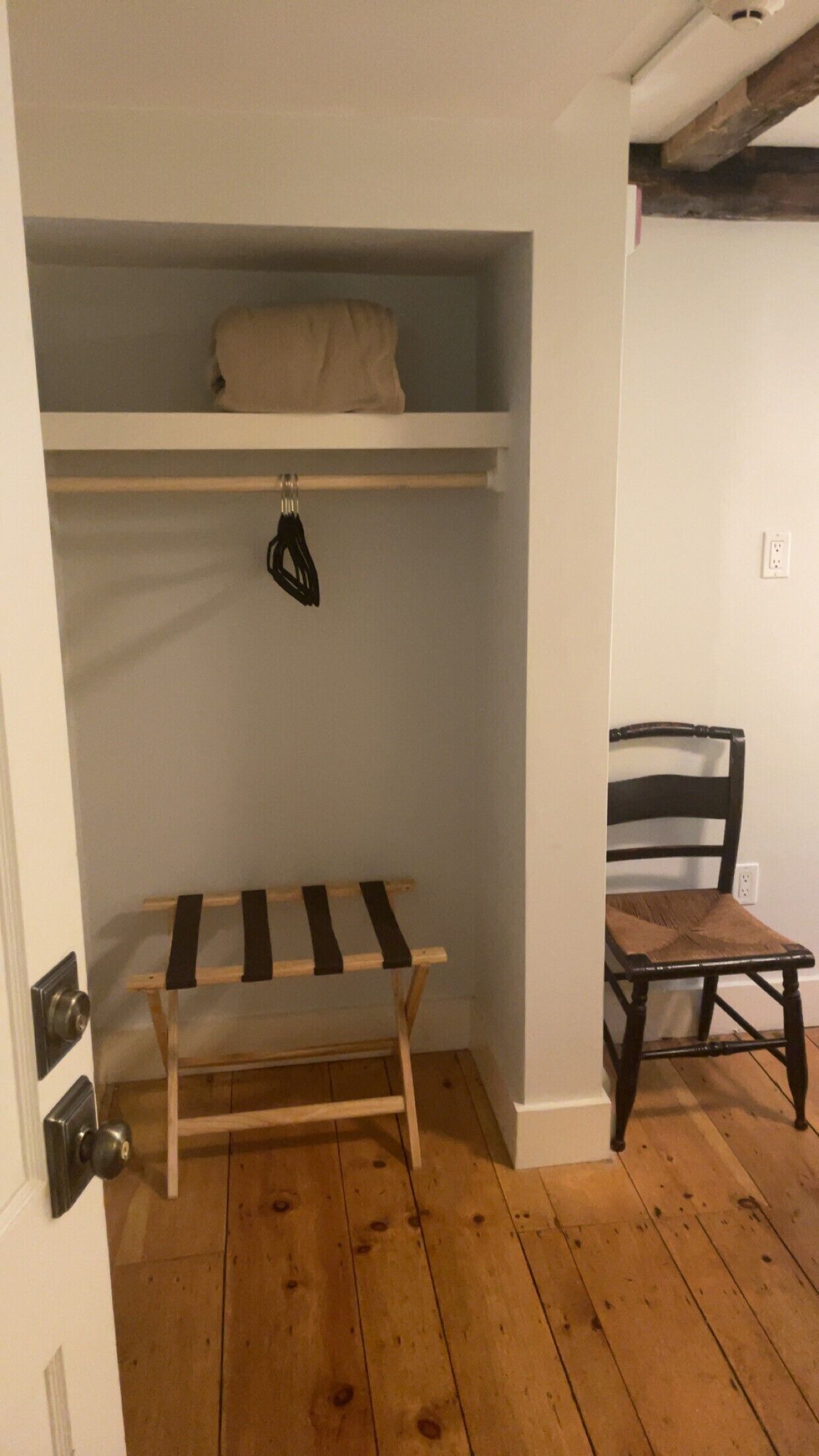 A room with a wooden bench, a chair, and a shelf with a bag.