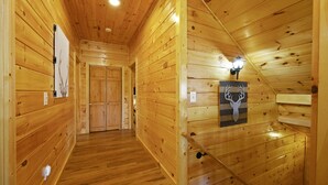 Ein Holzboden-Flur mit einer Holztür am Ende, einer Lampe an der rechten Wand und einer Dekoration eines Hirschkopfes.