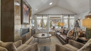 Een ruime woonkamer met een open haard, comfortabele zitplaatsen en een groot raam met uitzicht op het landschap.