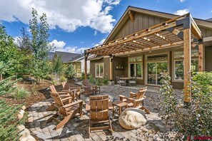 A covered patio area with wooden chairs and tables, surrounded by a garden with various plants and a stone pathway. - Hot Tub, Fireplace, 15 Minutes from Skiing! (Durango)