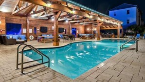 Un espace piscine intérieur avec des poutres en bois, une piscine et des fauteuils confortables.