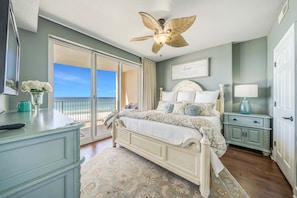 A bedroom with a bed, a nightstand, a dresser, a ceiling fan, and a view of the ocean.