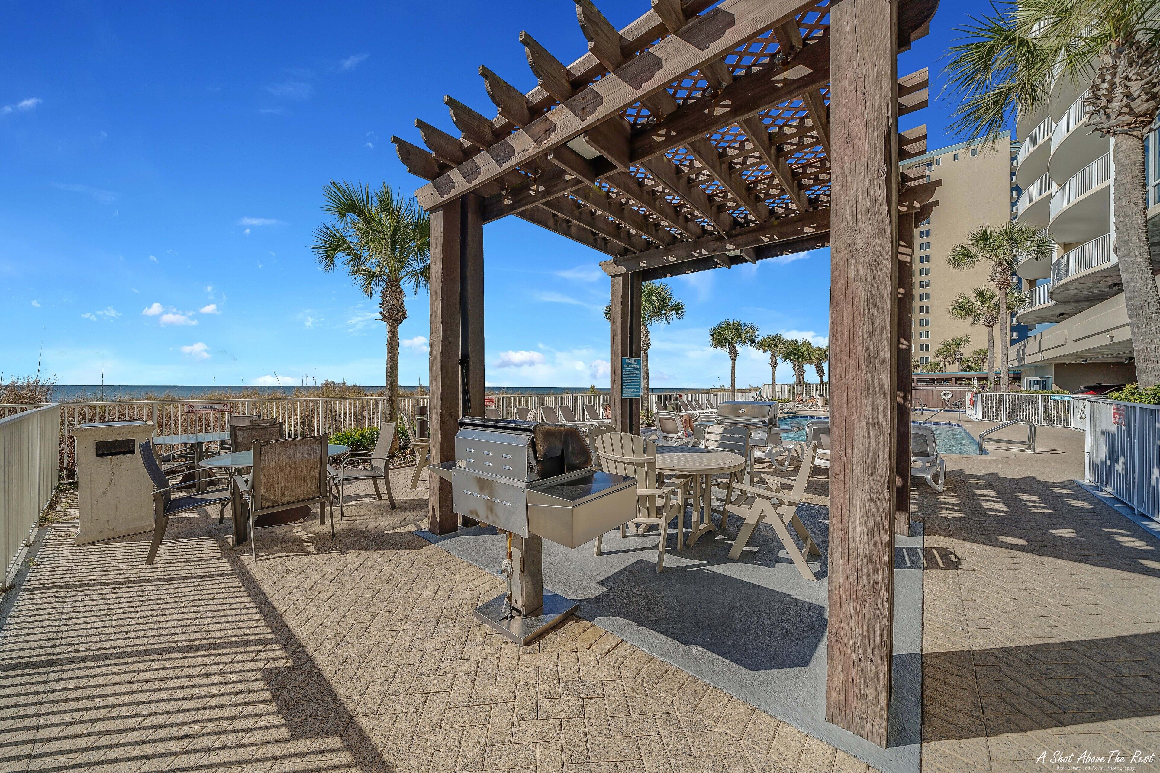 An outdoor patio area with a grill, tables, chairs, and a pergola.