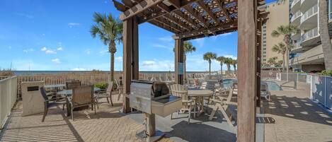 An outdoor patio area with a grill, tables, chairs, and a pergola.