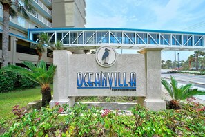 Une enseigne pour les condominiums Oceanvilla, avec un symbole d’oiseau, un pont piétonnier et une végétation luxuriante.