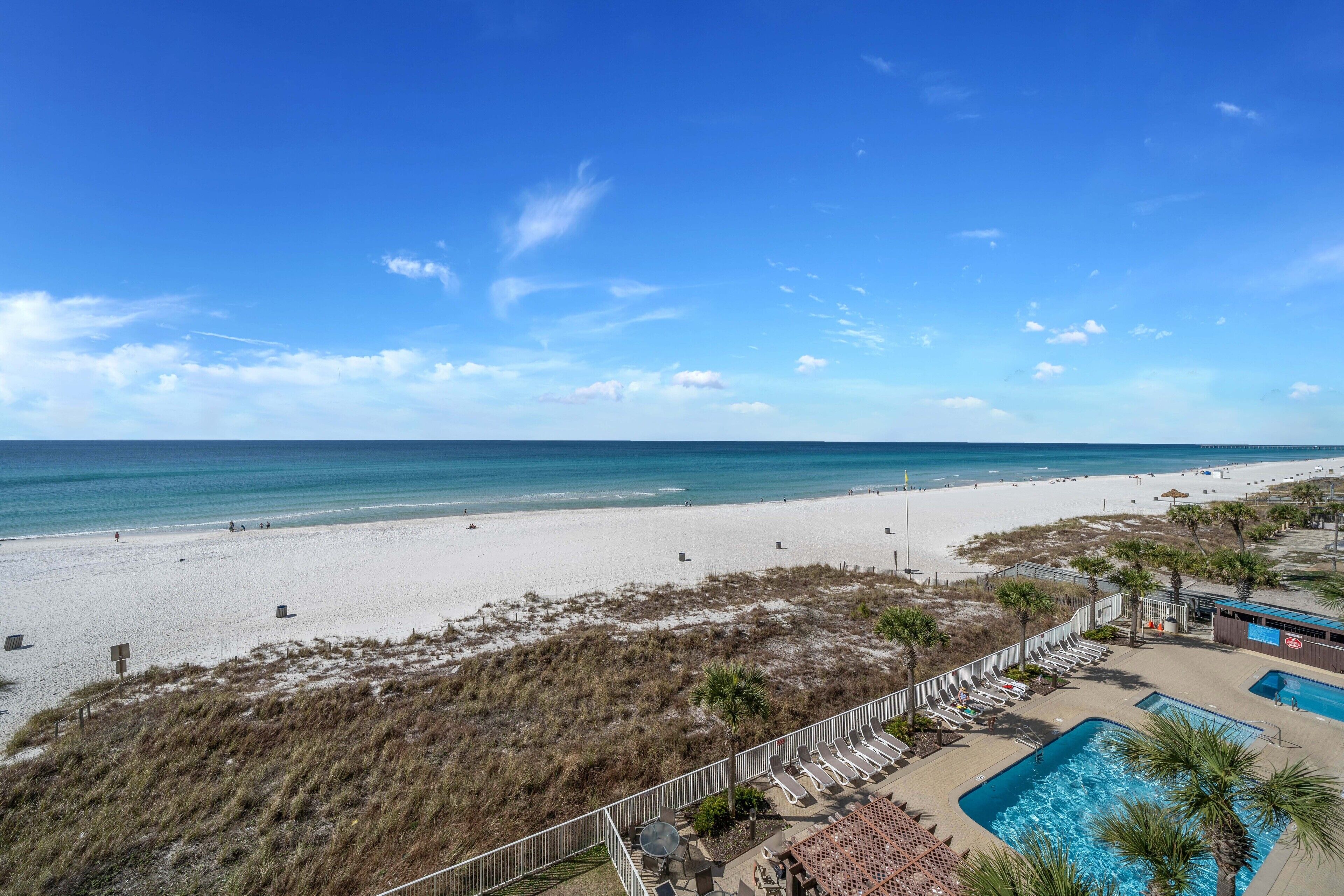 A beach resort with a swimming pool, lounge chairs, and a view of the ocean.