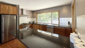 A modern kitchen with a stainless steel refrigerator, wooden cabinets, a large window, and a black granite countertop. - Grand Retreat in Mount Eliza (Mount Eliza)