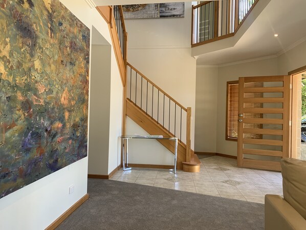 Un interior espacioso con una escalera, un cuadro abstracto grande y una puerta de madera.