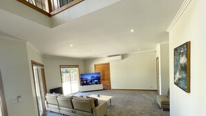 A spacious living room with a large flat-screen TV, a sofa, a coffee table, and a painting on the wall. - Grand Retreat in Mount Eliza (Mount Eliza)