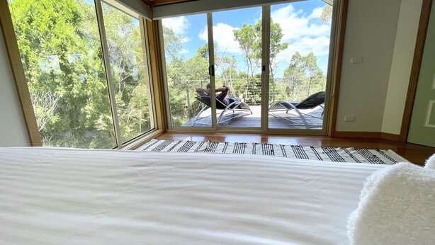 A bedroom with a large window overlooking a deck with two lounge chairs. - Grand Retreat in Mount Eliza (Mount Eliza)