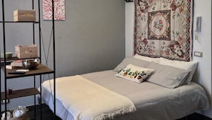 A bedroom with a bed, a wooden shelf unit, a patterned tapestry, and a small rug.