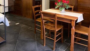 A dining area with a wooden table and chairs, a vase with red flowers, and a kitchen visible through an open door.