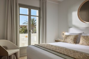 A hotel room with a bed, a chair, a nightstand, and a view of the outdoors. - Tzanis Resort (Skiros)