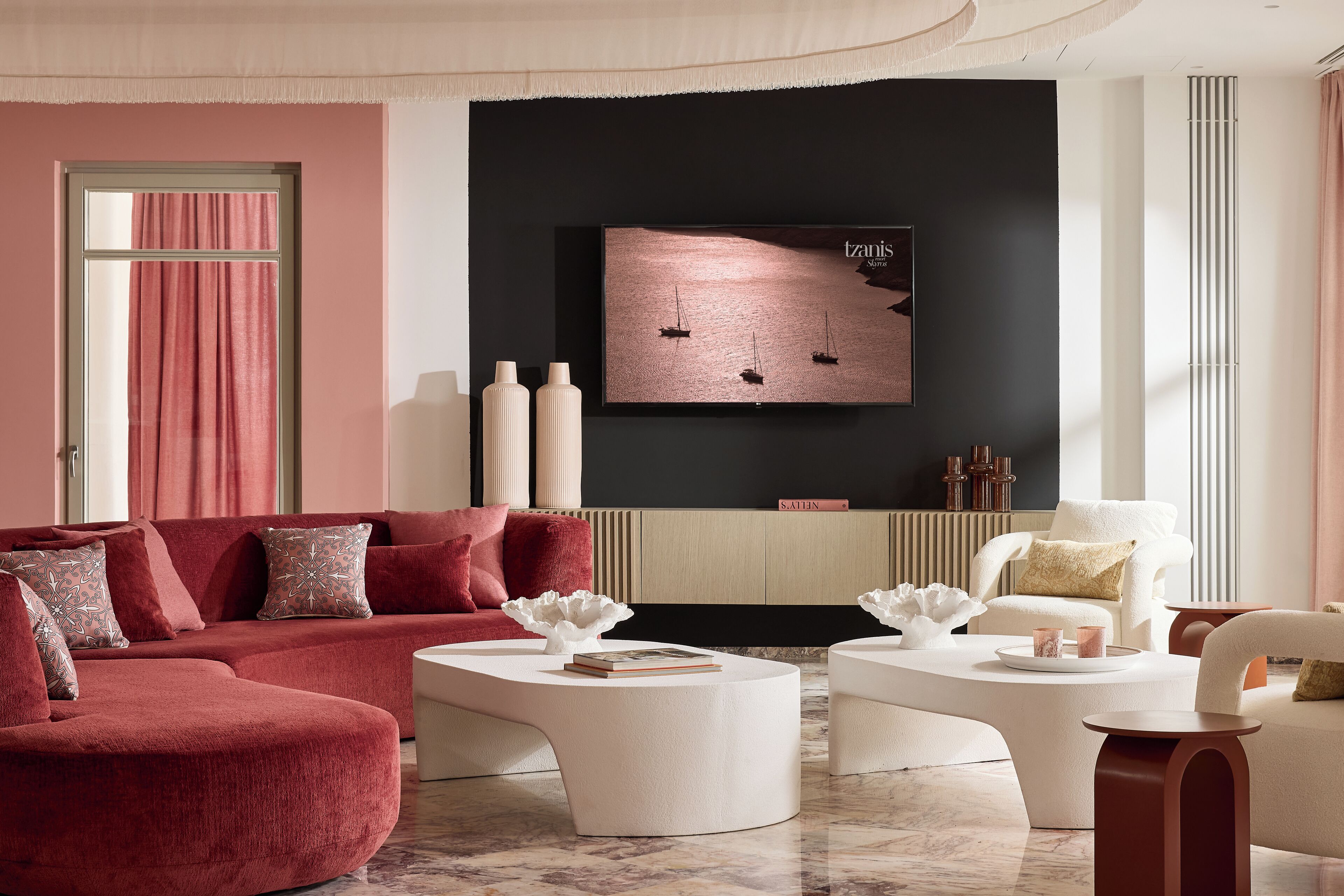 A modern living room with a red sofa, white coffee tables, and a flat-screen TV mounted on a black wall.