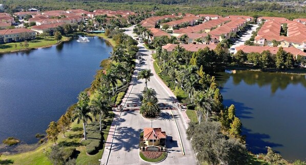 An aerial view of a residential area with houses, a central road, and a lake.