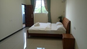 A clean, well-lit bedroom with a bed, a nightstand, a potted plant, and a window with curtains. - Sunshine Inn (Luganville)