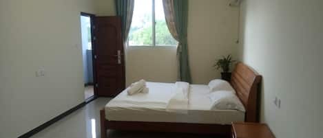 Un dormitorio limpio y bien iluminado, con cama, mesita de noche, planta en maceta y ventana con cortinas.