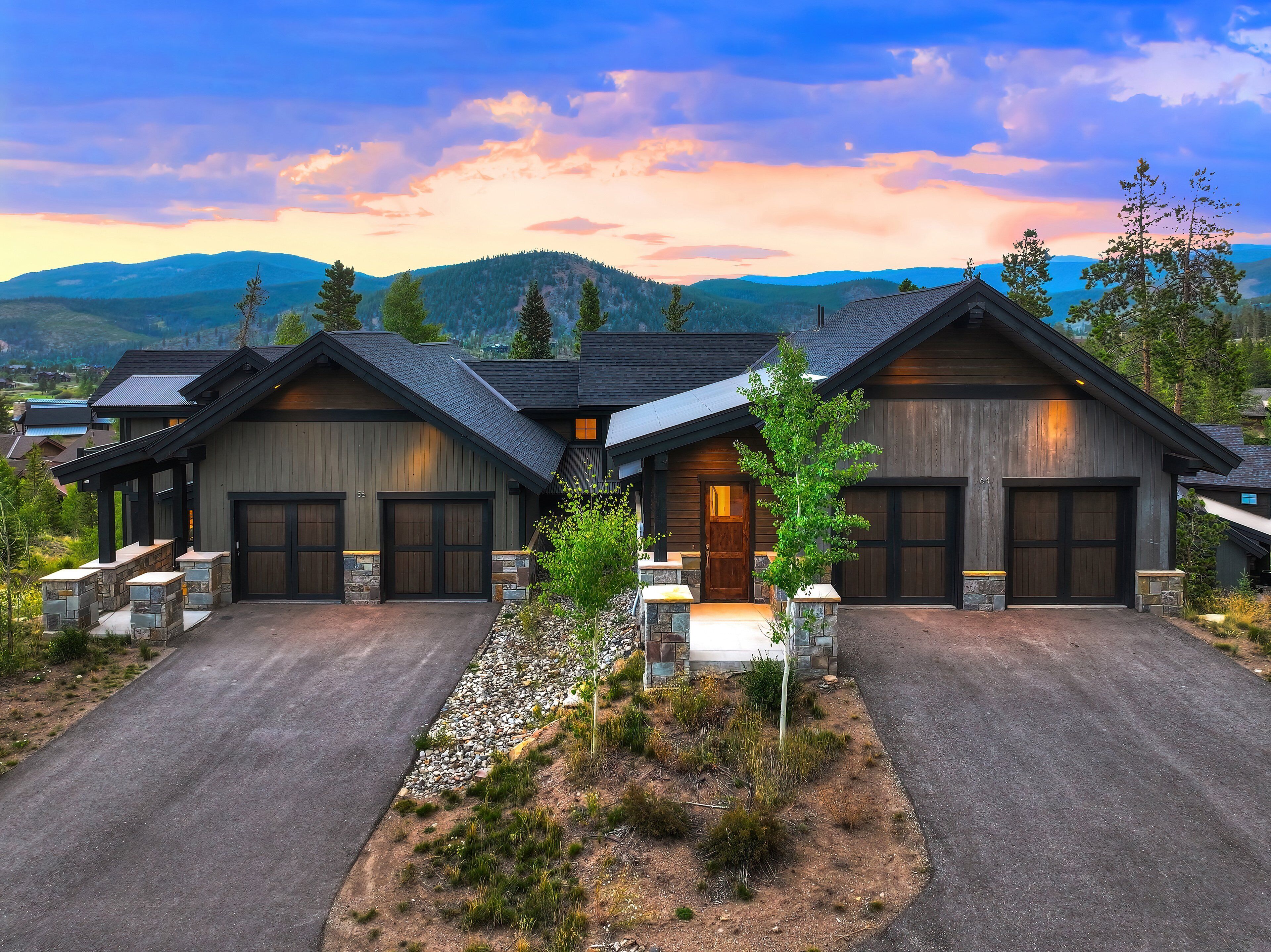A modern two-story house with a garage, stone foundation, and a driveway leading to a covered entrance.