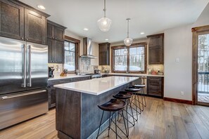 Una cocina moderna con armarios de madera oscura, electrodomésticos de acero inoxidable, una isla grande con taburetes y ventanas amplias con vistas al exterior.