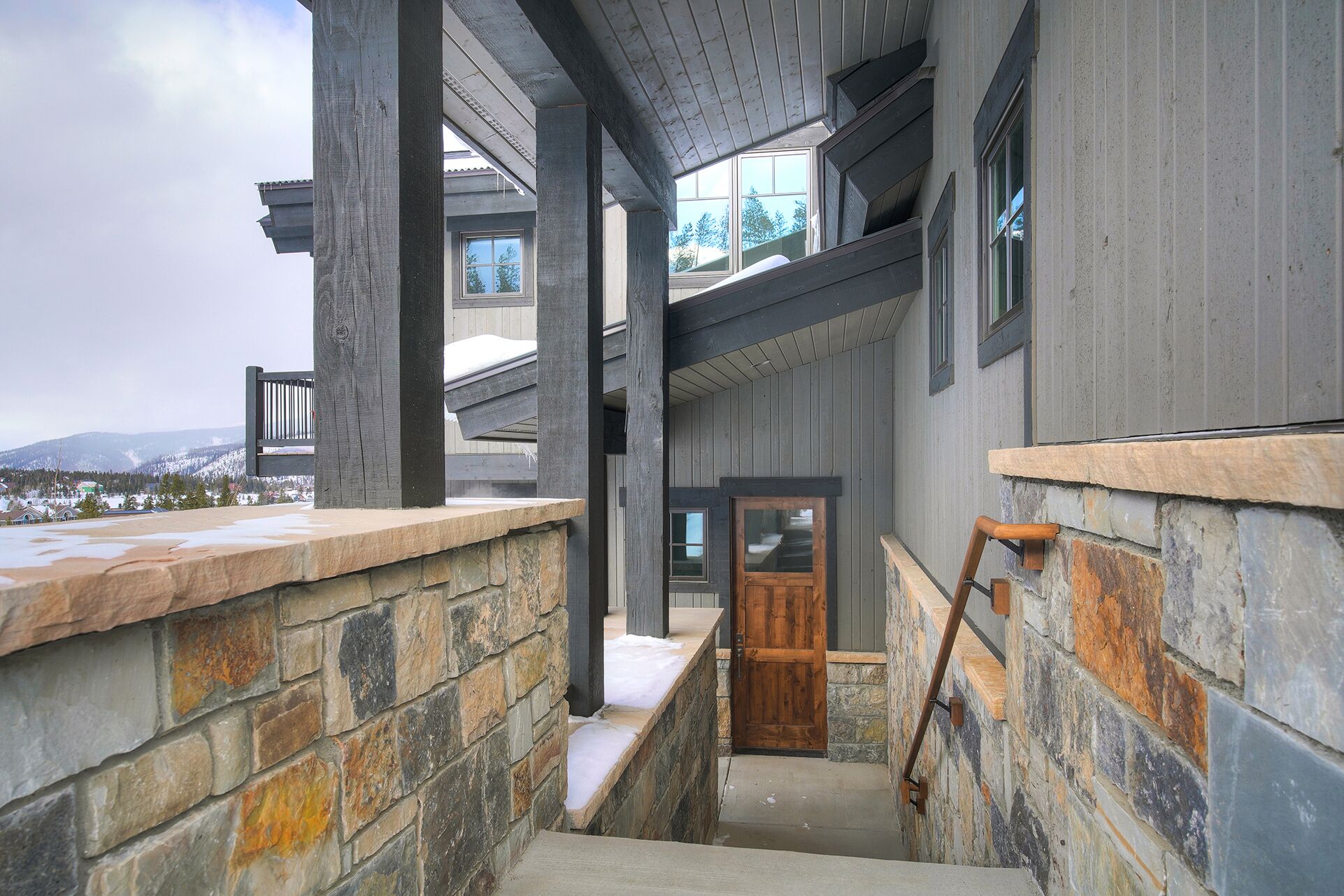 A wooden staircase leading to a door, with stone walls and a view of a snowy landscape.