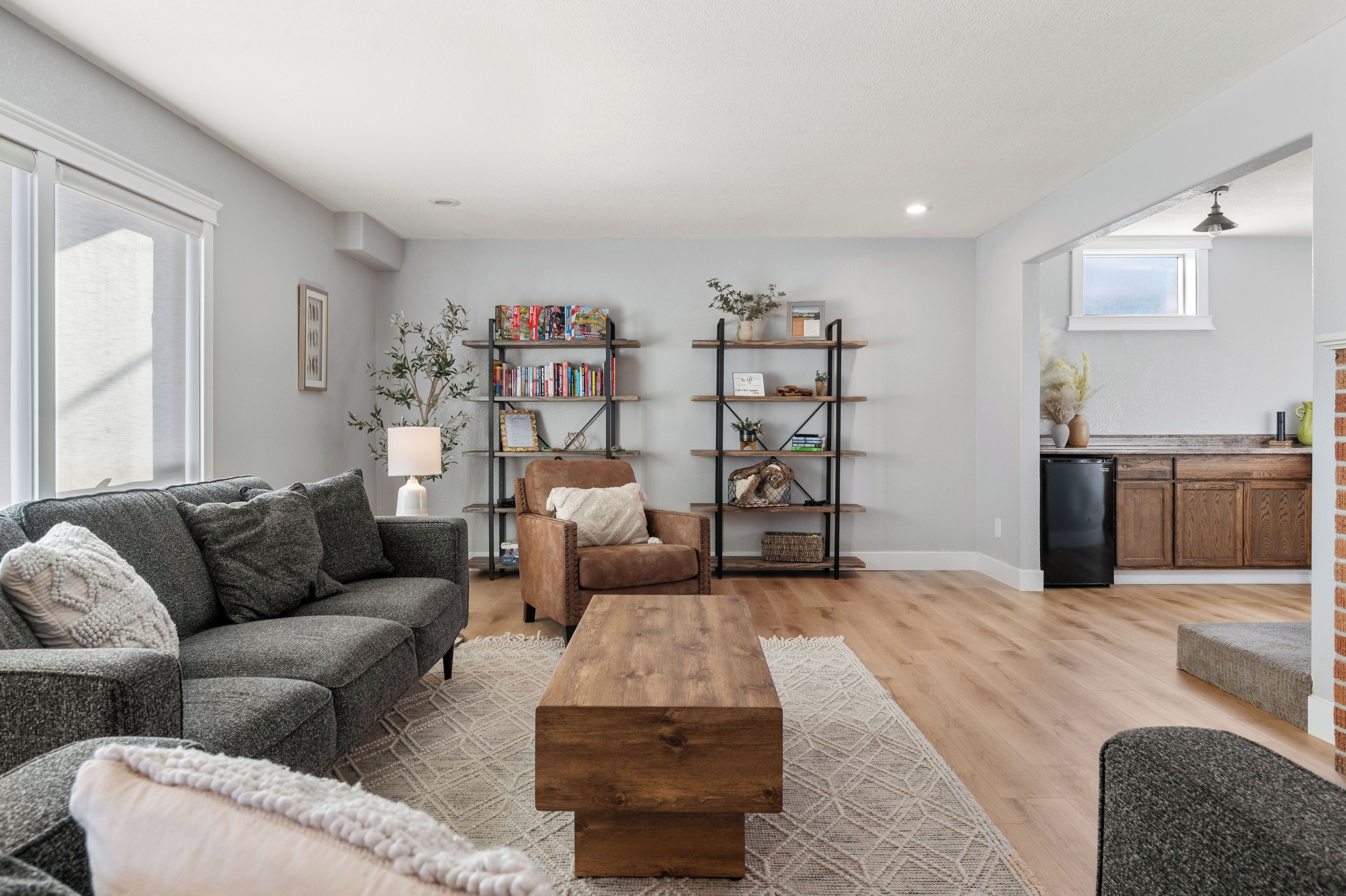 A spacious living room with a grey sofa, a wooden coffee table, and a bookshelf filled with books and decorative items.