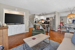 A modern kitchen with white cabinets, a flat-screen TV, and a dining area with a table and chairs.