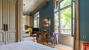 Hotelkamer met een groot bed, een eettafel met stoelen, een bank en een raam met uitzicht op bomen.