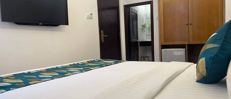A hotel room with a bed, a flat-screen TV mounted on the wall, a wardrobe, and an air conditioning unit.