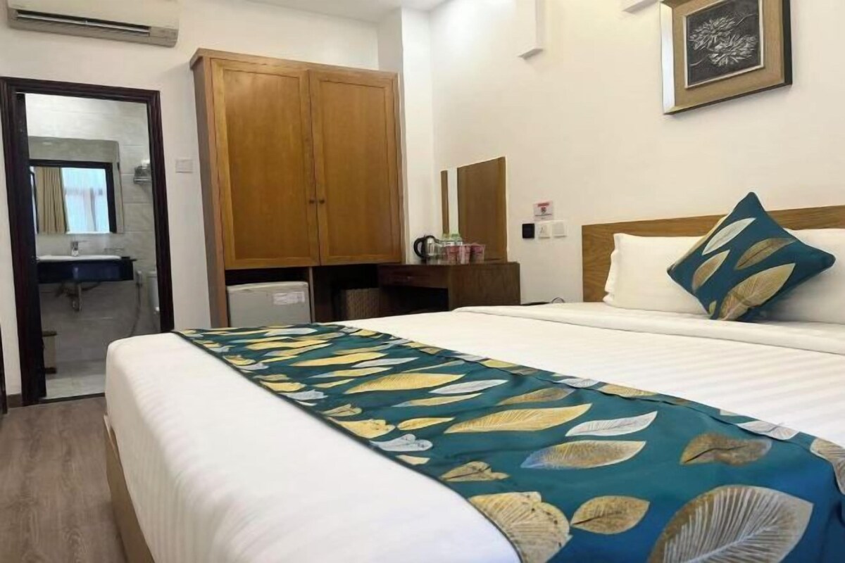 Habitación de hotel con cama, armario de madera, escritorio pequeño con espejo y un cuadro en la pared.