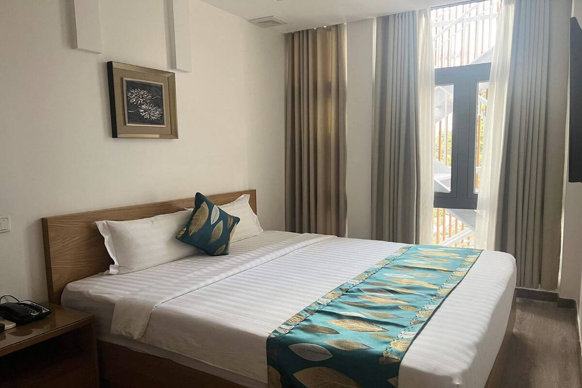 A neatly made bed with a blue and white patterned bedspread, a wooden headboard, and a single pillow with a leaf design.