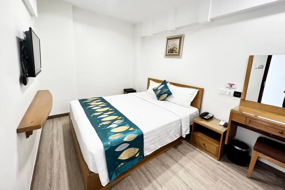 A hotel room with a bed, bedside table, desk, chair, and a mirror.