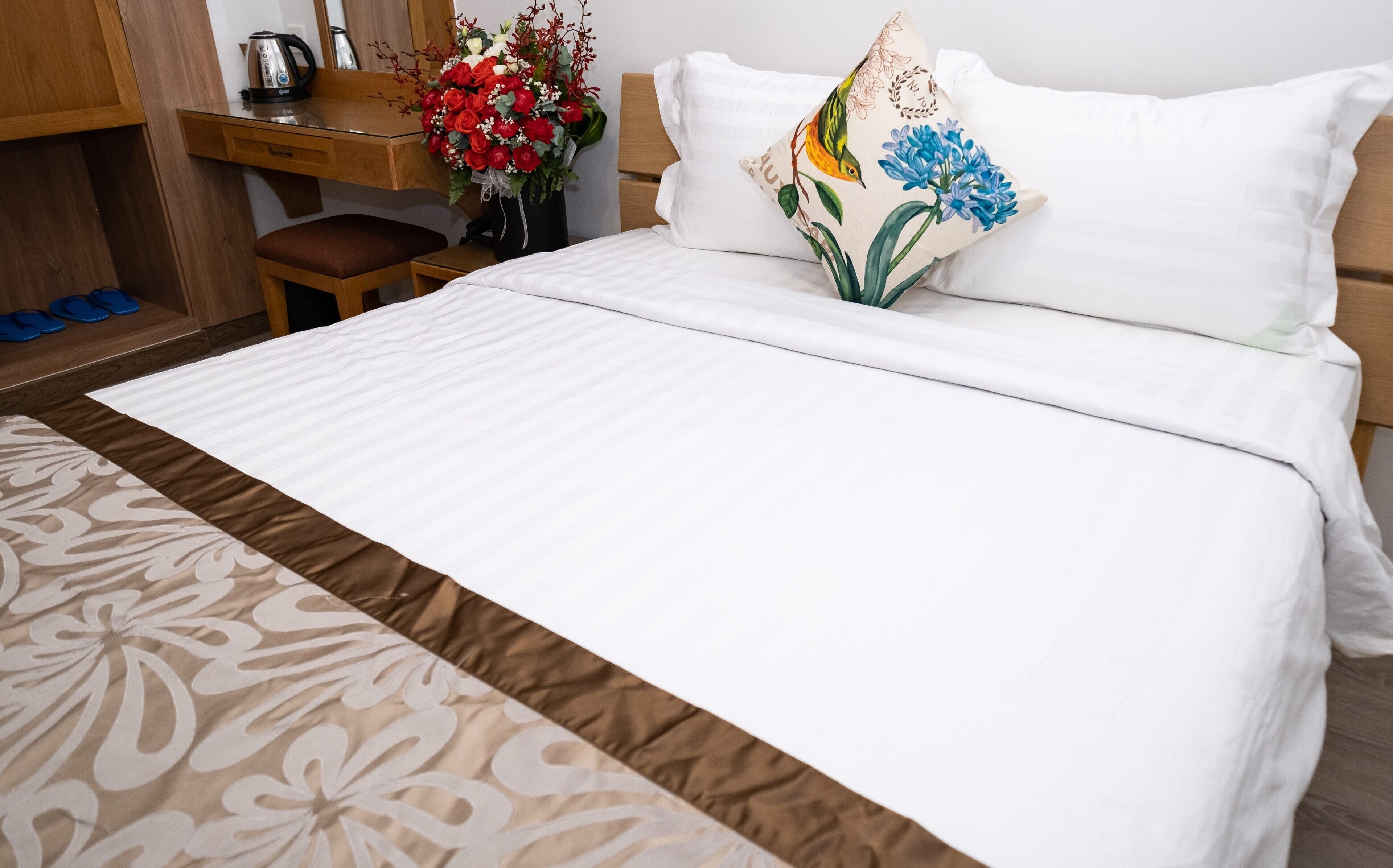 Un lit bien fait, avec une literie blanche, un plaid à motifs et un coussin décoratif orné de motifs floraux.