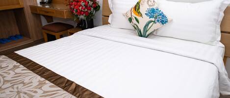 Un lit bien fait, avec une literie blanche, un plaid à motifs et un coussin décoratif orné de motifs floraux.