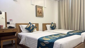 Habitación de hotel con dos camas, un escritorio y una silla. Hay un cuadro en la pared y una ventana con cortinas.