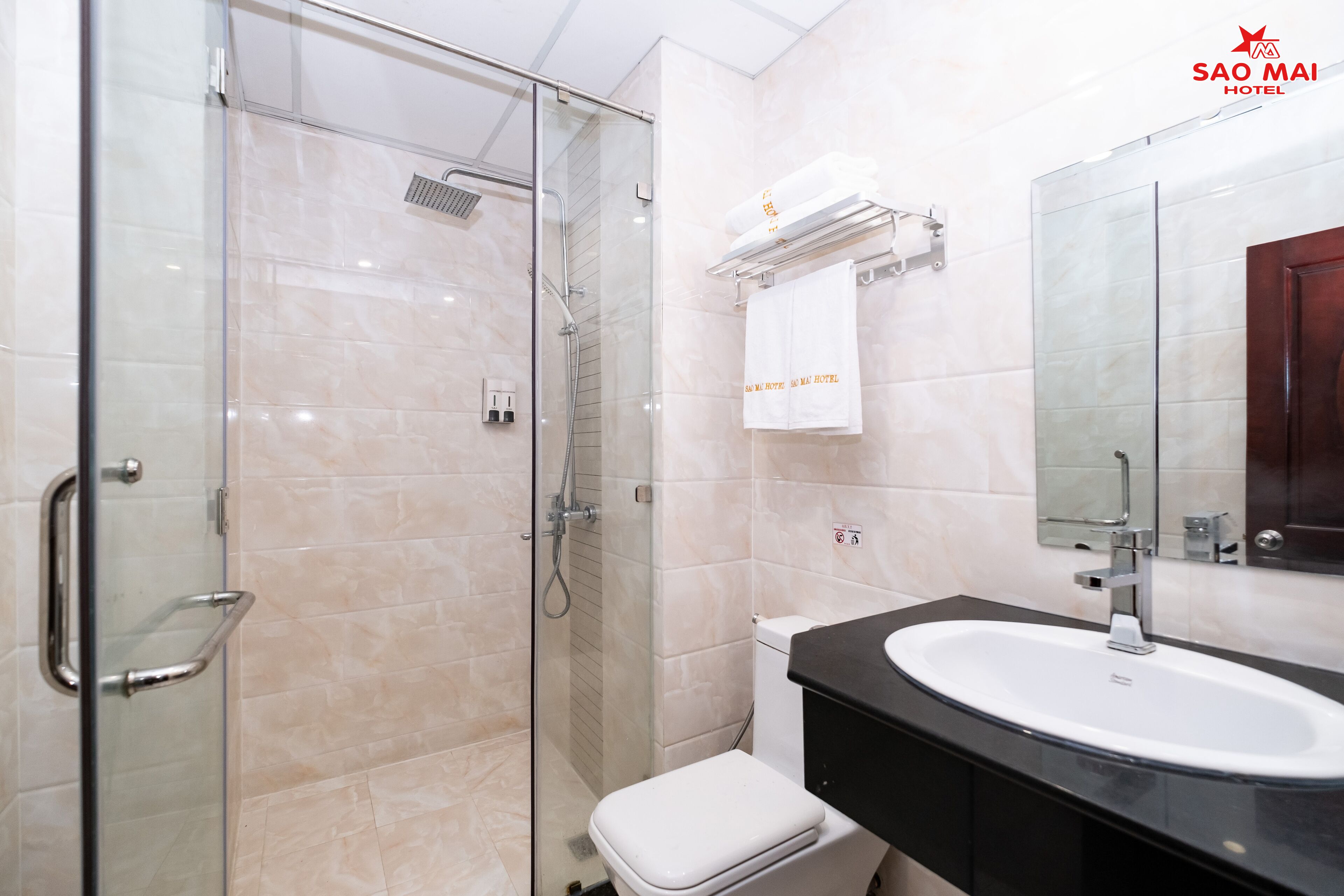 Un baño moderno con cabina de ducha de vidrio, inodoro blanco, lavamanos negro y espejo sobre el lavamanos.