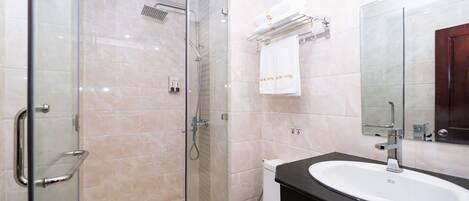 Un baño moderno con cabina de ducha de vidrio, inodoro blanco, lavamanos negro y espejo sobre el lavamanos.