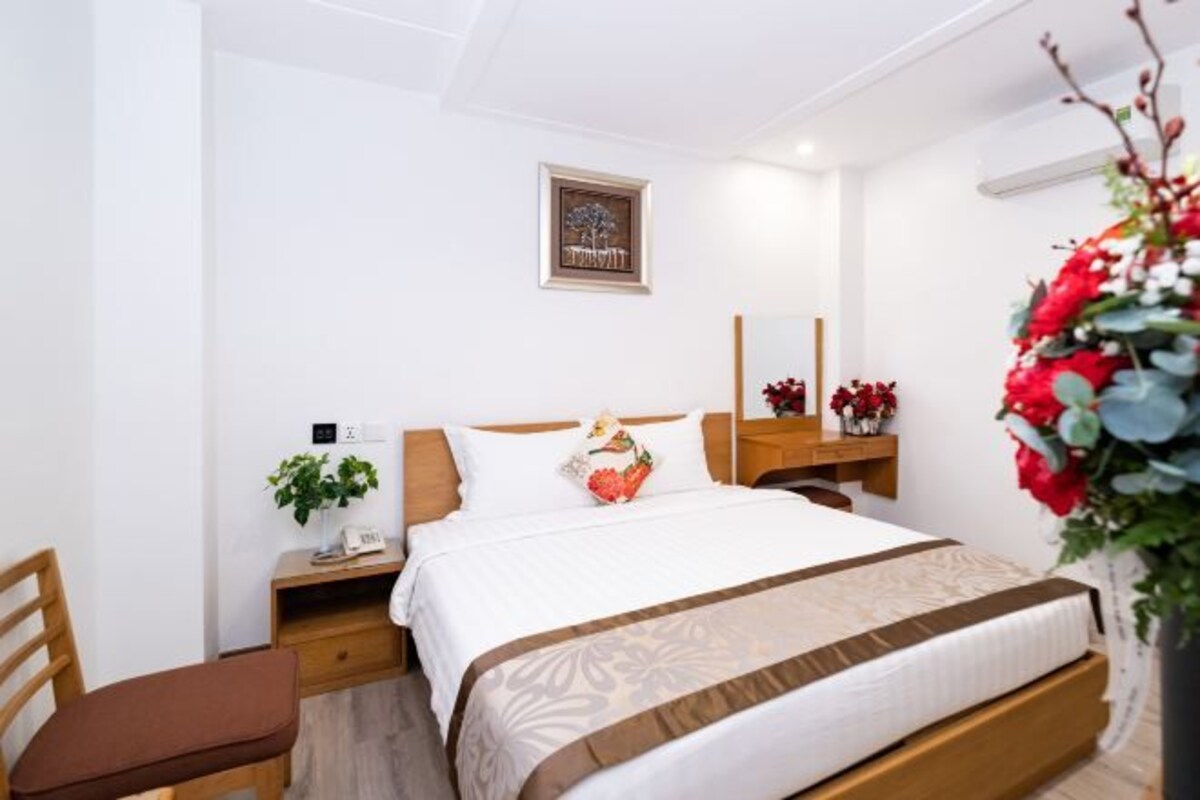 Un dormitorio ordenado con cama, mesita de noche, silla y espejo montado en la pared.