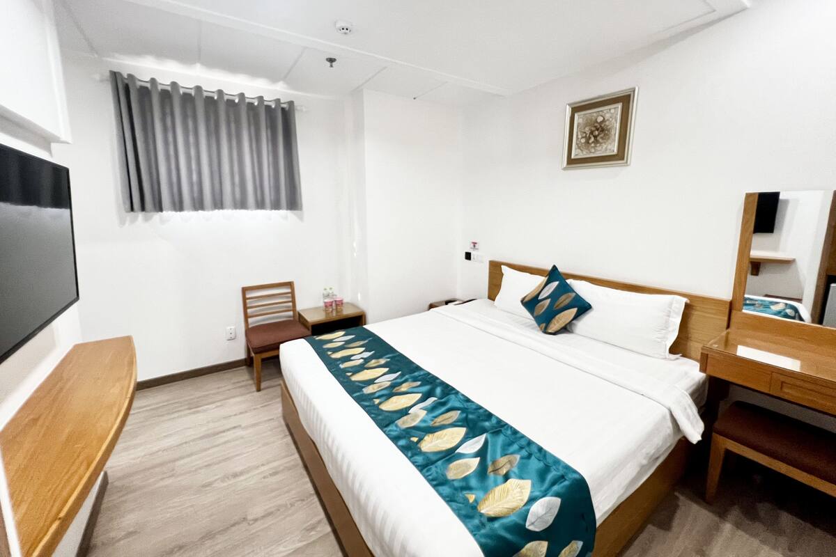 A hotel room with a bed, bedside table, TV, and a window with curtains.