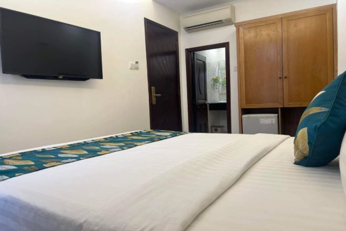 Habitación de hotel con una cama, un televisor de pantalla plana en la pared, un armario y un equipo de aire acondicionado.