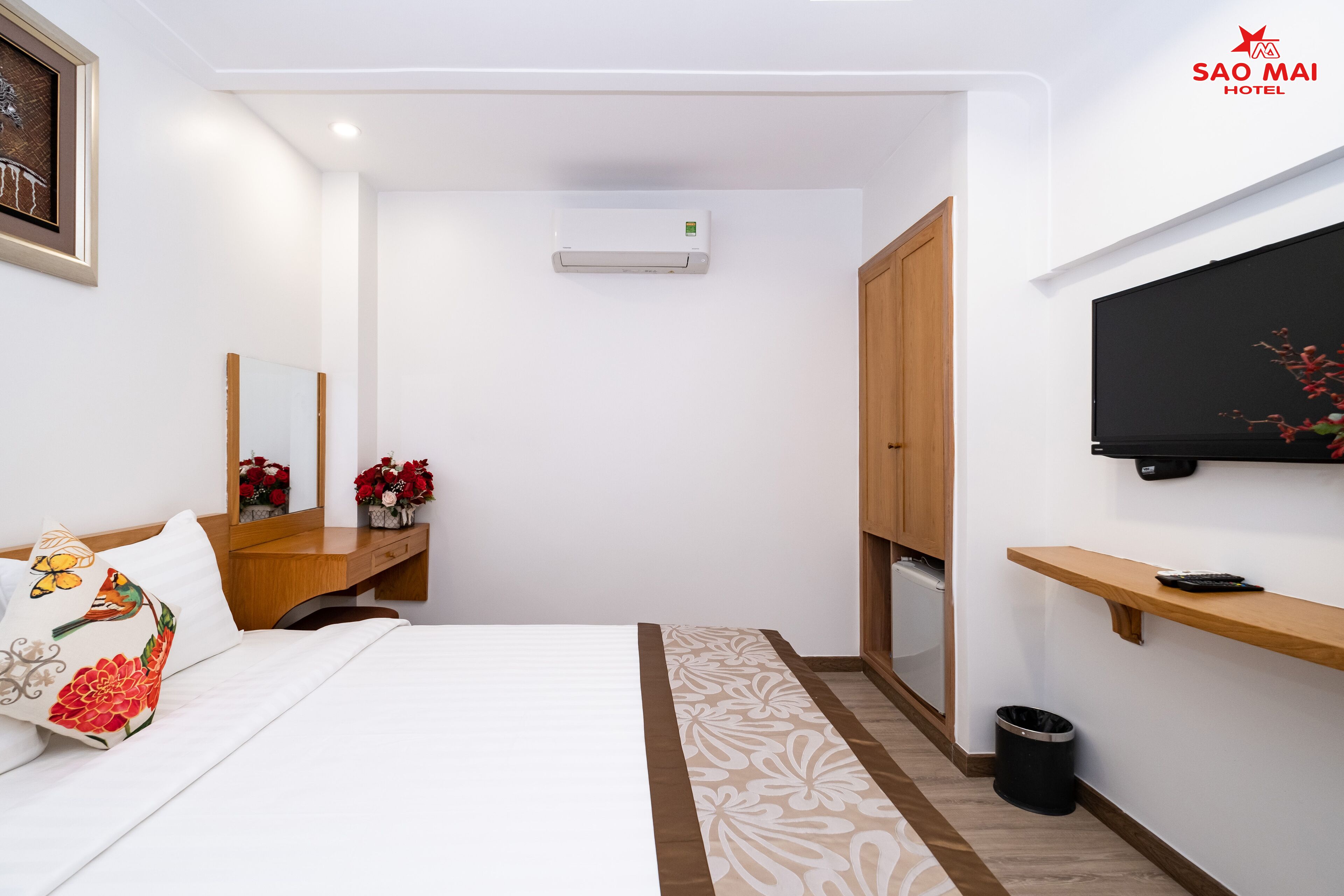 A hotel room with a bed, a wooden desk, a mirror, a TV, and a wardrobe.