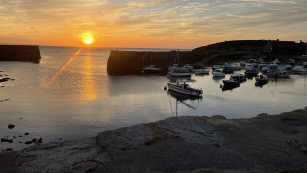 A coastal sunset with boats docked at a harbor, a stone wall, and a building in the background. - L'Odyle - House for 6 people 1 Km from the sea (Fermanville)