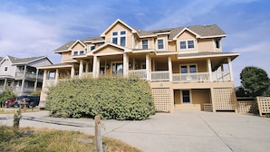 A multi-story residential building with a balcony on the second floor, a covered front porch, and a small front yard with a bush. - LUXURY, OCEANFRONT, Pool, ELEV, Rec Rm, Beach Access, Ocean Views! WL983, Fairlight (Corolla)